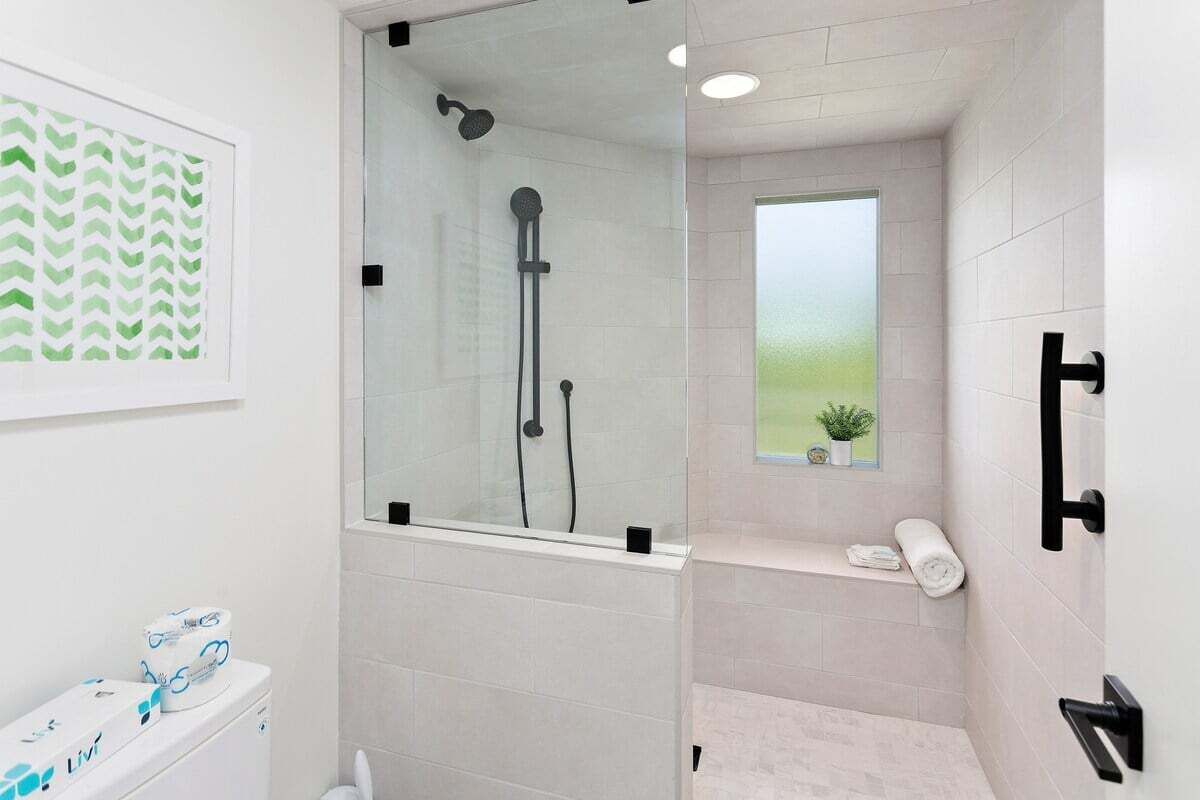 A modern bathroom with a glass-enclosed shower, a toilet with a visible brand, a small window with a plant, and a shelf with towels.