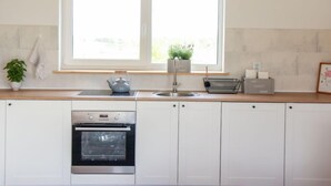 A modern kitchen with white cabinets, a built-in oven, a sink, and a window above the counter. - Dom Przy Cisowym Jarze by Interhome (Jablonowo)