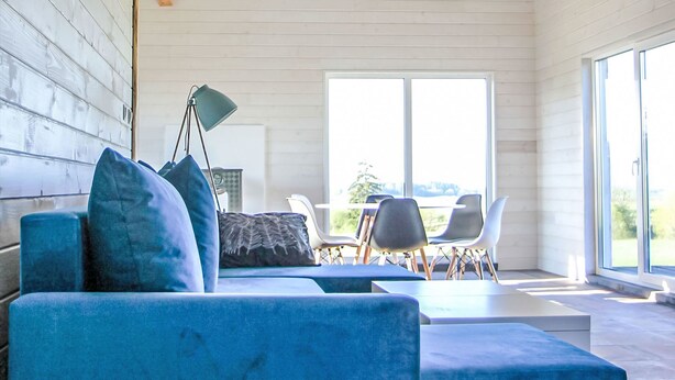 A modern interior with a blue sofa, a table with chairs, and a large window providing a view. - Dom Przy Cisowym Jarze by Interhome (Jablonowo)