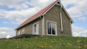A single-story house with a red roof, large windows, and a grassy hill in the foreground. - Dom Przy Cisowym Jarze by Interhome (Jablonowo)