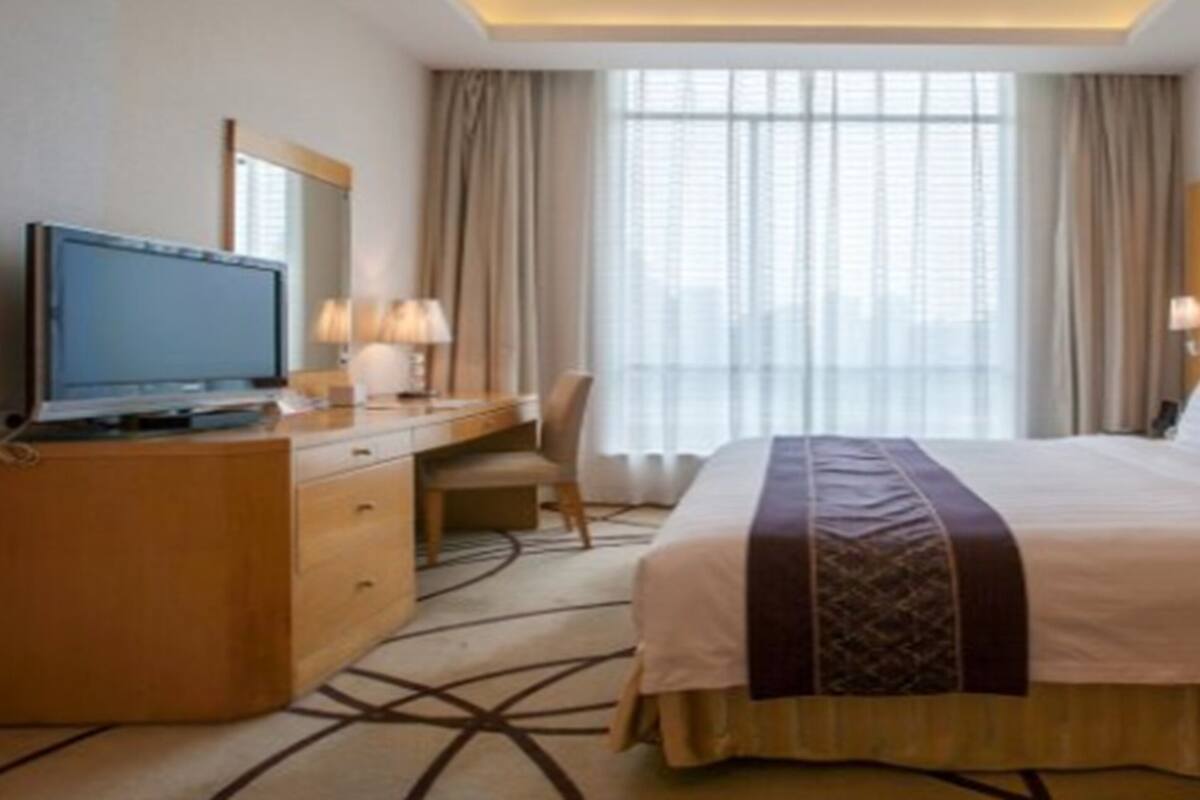 A hotel room with a large bed, a desk with a computer, a chair, and a window with curtains.