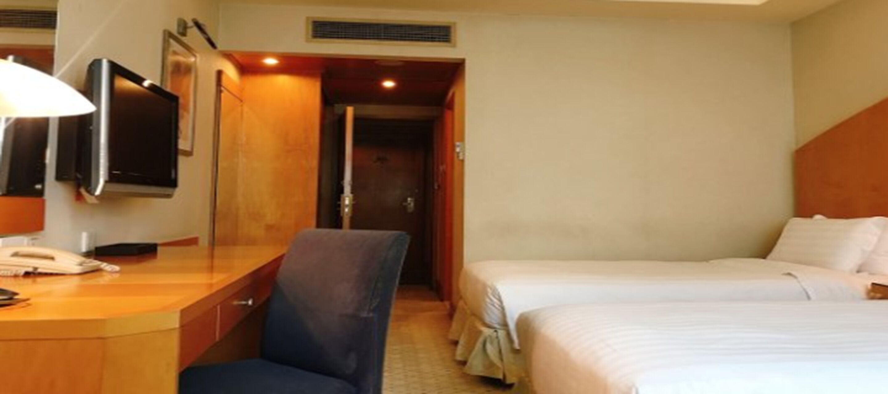 A hotel room with a desk, chair, two beds, and a television.