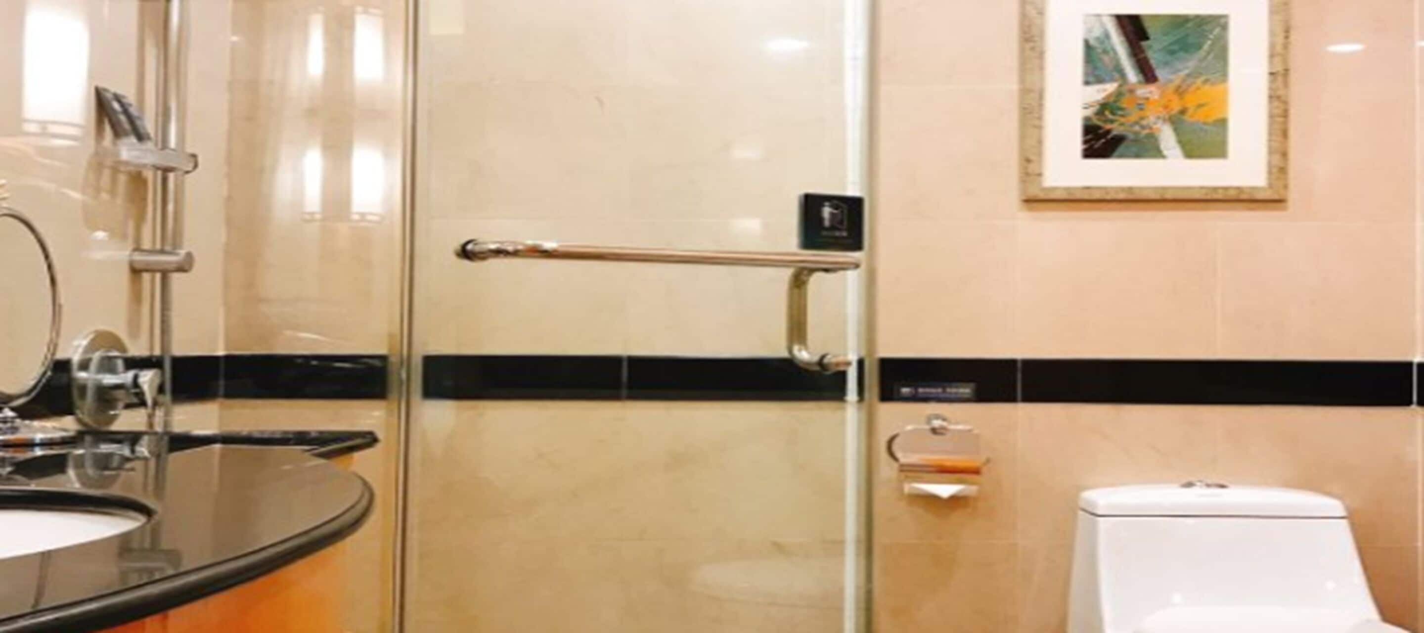 Un baño moderno con mampara de ducha de vidrio, lavamanos con encimera negra, inodoro blanco y un cuadro abstracto enmarcado en la pared.