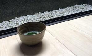 A ceramic bowl with green liquid on a wooden surface, next to a gravel path. - Ichijyo PREMIUM (Kyoto)