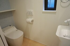 A small bathroom with a toilet, a wall-mounted bidet, a sink, and a window. - Ichijyo PREMIUM (Kyoto)