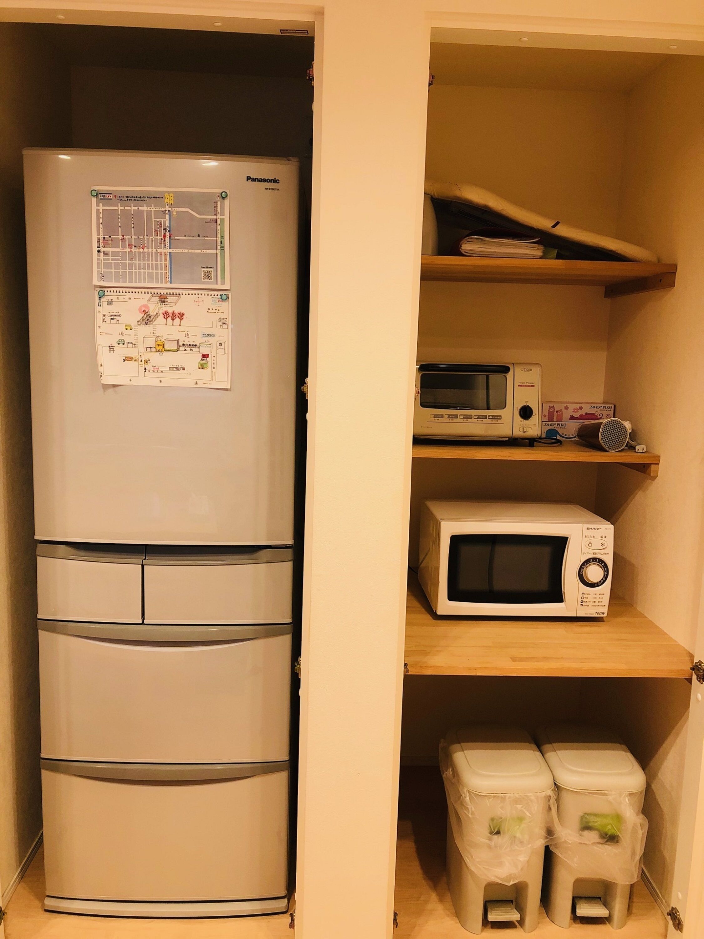 Una cocina compacta con refrigerador, microondas y dos cubetas de basura.