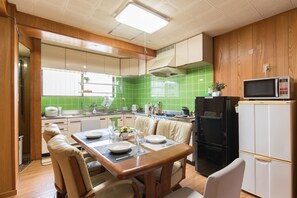 A compact kitchen with a dining area, wooden cabinets, a microwave, and a refrigerator. - Naha House (Naha)