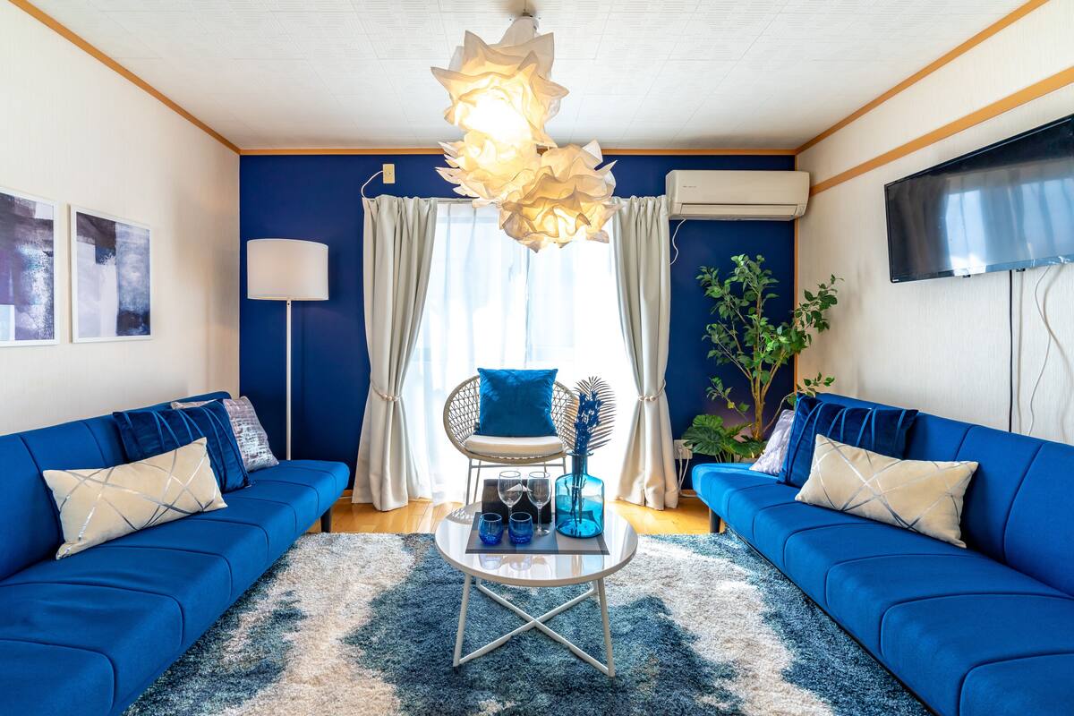 A living room with two blue sofas, a round coffee table, a modern chandelier, and a large window with curtains.
