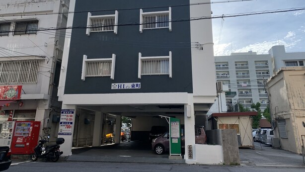 A multi-story building with a dark facade and white window frames, featuring a sign with Japanese characters. - Naha House (Naha)