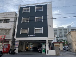 A multi-story building with a dark facade and white window frames, featuring a sign with Japanese characters. - Naha House (Naha)