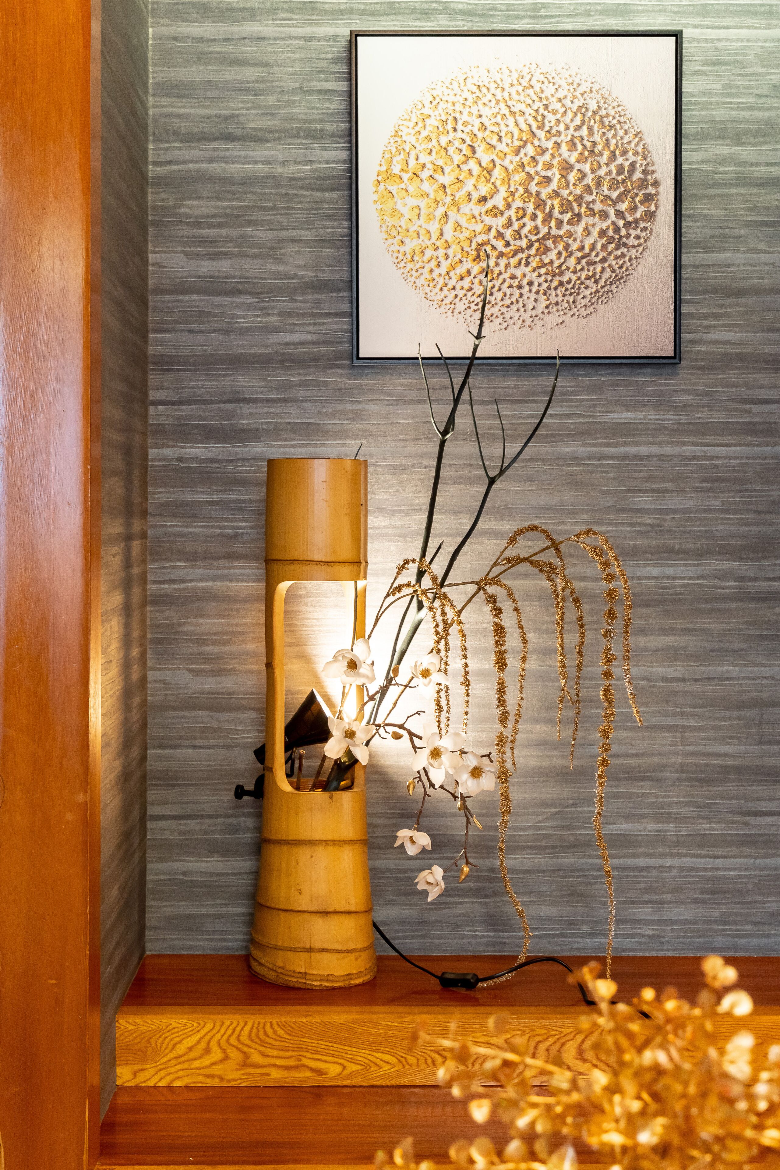 A room with a wooden floor, a cylindrical lamp, and a framed artwork on the wall.
