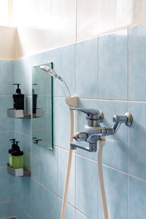 A bathroom with a shower, a mirror, and toiletries on a shelf. - Naha House (Naha)