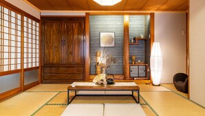 A traditional Japanese room with tatami flooring, a low table with a fan and tea set, a shoji screen door, and a sliding door. - Naha House (Naha)