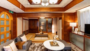 A traditional Japanese-style room with tatami flooring, a low wooden table, a sofa with cushions, and a television on a cabinet. - Naha House (Naha)