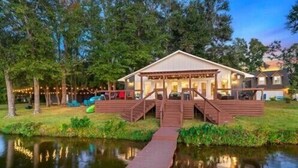 A cabin with a wooden deck and a dock leading to a pond, surrounded by trees. - 5 STAR VIEWS! Boat rental! Chef's kitchen! SUP/kayak/game room/mauimat (Murchison)