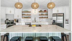 A modern kitchen with white cabinets, a marble island, and three hanging wicker pendant lights. - 5 STAR VIEWS! Boat rental! Chef's kitchen! SUP/kayak/game room/mauimat (Murchison)