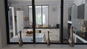 Cozinha moderna com armários brancos, área de refeições com mesa posta para dois e vista através de uma grande janela.