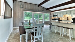 Una cocina con comedor, vigas de madera, ventanas amplias y vista a zonas verdes.