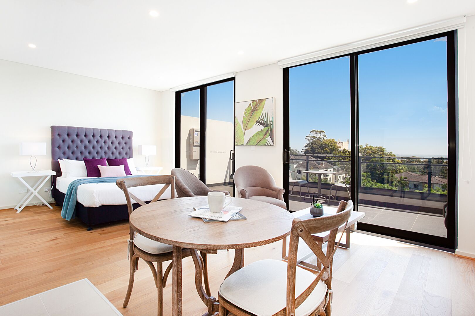 Una habitación de hotel moderna con una cama grande, una mesa de comedor y un balcón con vistas a la ciudad.