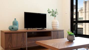 Una sala de estar moderna con un mueble bajo para televisor de madera, un televisor de pantalla plana, un florero con plantas verdes y una pequeña mesa con una planta en maceta.