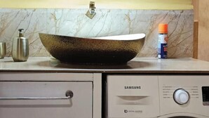 Une salle de bain avec un lavabo en marbre, un miroir, un lave-linge et un meuble de rangement.