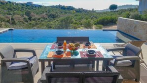 An outdoor dining area with a table set for two, overlooking a swimming pool and a scenic hillside view. - Villa Belios by Interhome (Porto Vecchio)