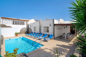 A swimming pool with blue water, surrounded by lounge chairs and a table.