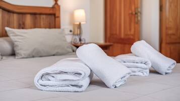 A neatly made bed with folded white towels, a wooden headboard, a bedside lamp, and a wooden door in the background.