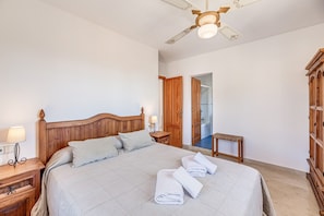 Une chambre à coucher avec un lit en bois, des lampes de chevet, un ventilateur de plafond et une armoire en bois.