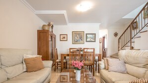 Una sala de estar con sofá, una mesa de comedor con sillas, un aparador de madera y una escalera.