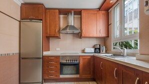 Una cocina moderna con armarios de madera, un refrigerador de acero inoxidable, un horno y un ventanal que proporciona luz natural.