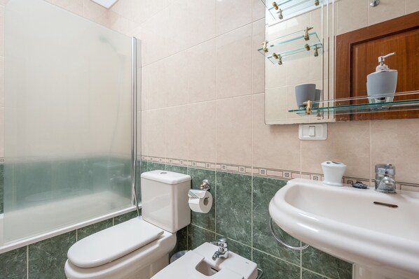 Une salle de bain dotée d’une douche à parois de verre, de toilettes, d’un bidet, d’un lavabo et d’un miroir avec des étagères en verre.
