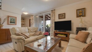 Una sala de estar con un sofá, una mesa de centro de vidrio, un televisor y un ventanal corredizo que da a un espacio exterior.