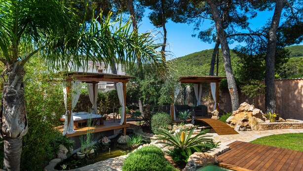 A pool area with wooden deck, two wooden gazebos, and a small pond.