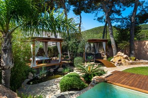 Zona de piscina con cubierta de madera, dos gazebos de madera y un estanque pequeño.