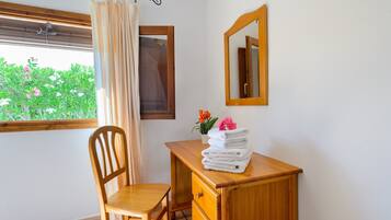 Een kamer met een houten bureau, een stoel, een raam met uitzicht op groen, een spiegel en een gordijn.