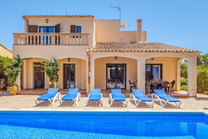 A two-story house with a swimming pool, sun loungers, and a covered patio.