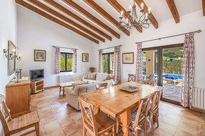 Ampla sala de estar com mesa de jantar de madeira, sofá e aparador para televisão.