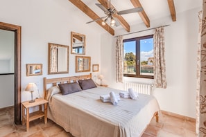 A bedroom with a bed, wooden headboard, ceiling fan, and a window with curtains.