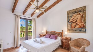 A bedroom with a bed, a wooden ceiling fan, a wicker chair, a painting on the wall, and a view through a glass door. - Vacation Home Villa Karen with Pool & Wi-Fi (Sa Rapita)