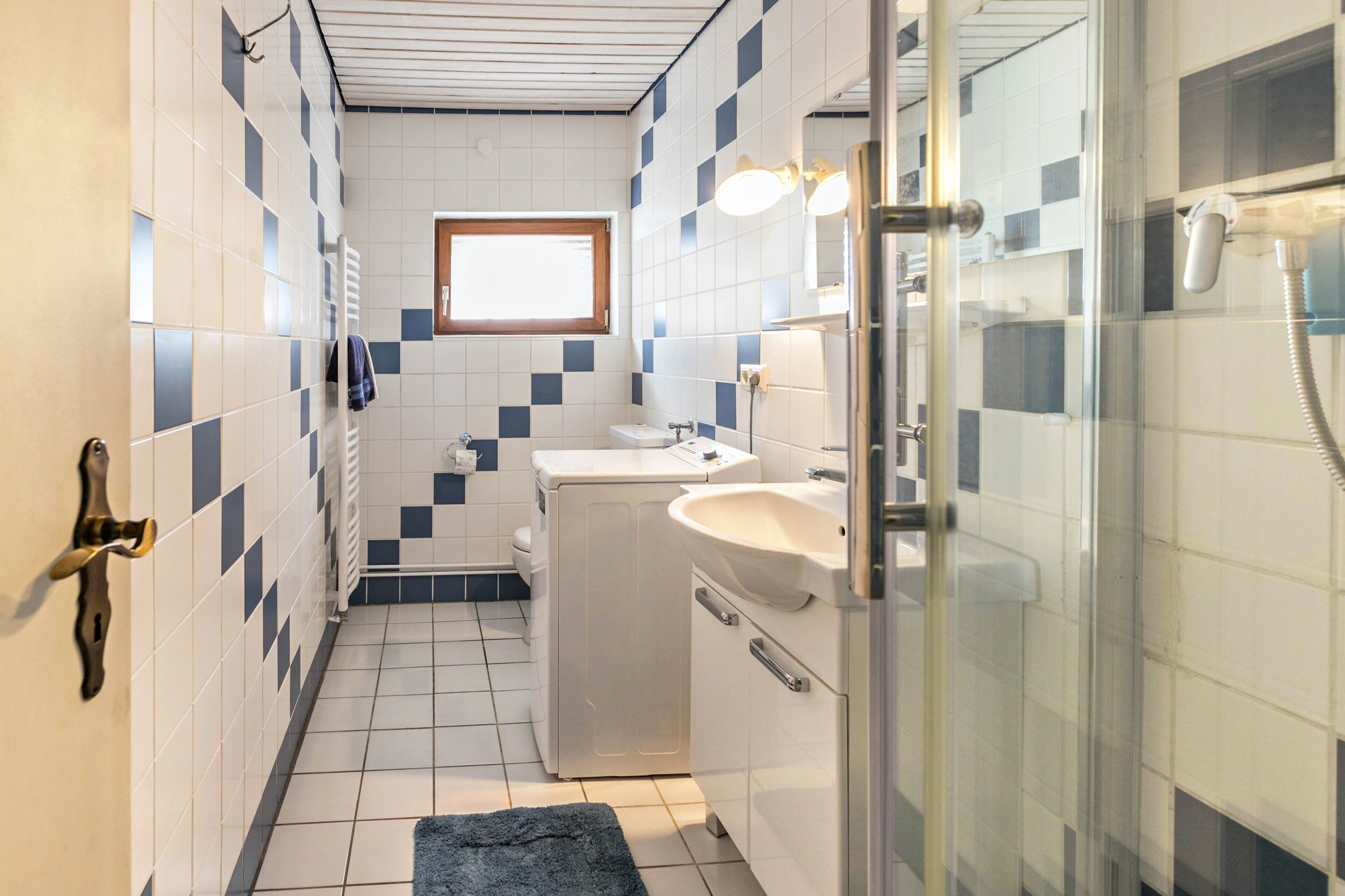 A bathroom with a tiled floor, a sink, a mirror, a towel rack, and a shower.