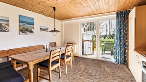 Ein Holztisch mit Stühlen, einer Bank und einer Pendelleuchte in einem Raum mit gefliestem Boden und Holzbalkendecke.