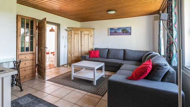 Un salon comprenant un canapé, une table basse, un meuble en bois et une porte donnant sur une autre pièce.