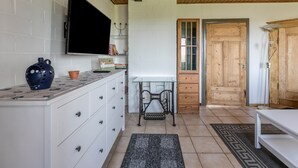 Une cuisine avec des meubles blancs, un téléviseur fixé au mur, une porte en bois et un banc.