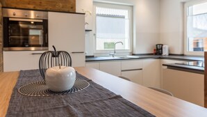A modern kitchen with a built-in oven, a window with a view, and a dining table with a white bowl. - Holiday Apartment "Roderer" with Mountain View, Wi-Fi, Balconies & Terrace (Völs)