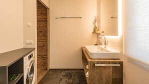 A modern bathroom with a built-in washing machine, a wooden vanity, and a large mirror. - Holiday Apartment "Roderer" with Mountain View, Wi-Fi, Balconies & Terrace (Völs)