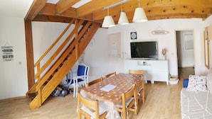 A cozy room with a wooden staircase, a dining table with chairs, a sofa, a TV, and a white cabinet.