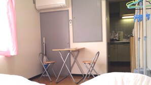 A hotel room with two beds, a small table, two foldable chairs, a door, and a view into the kitchen area. - Gojyo-IVY Twin bed 2 (Kyoto)