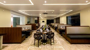 A modern dining area with a central round table, booths, and a high ceiling with linear lighting. - The Fern Residency, Vijayapura (Bijapur)