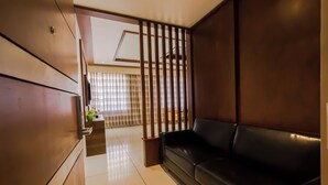A modern living room with a black leather sofa, wooden paneling, and a view through a wooden partition to a balcony with a window. - The Fern Residency, Vijayapura (Bijapur)